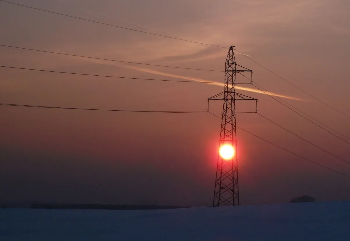 Setting sun aligned inside a power pylon over a snowy horizon